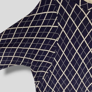 May include: Navy blue sweater with a white diamond pattern. The sweater has long sleeves and a crew neck. The argyle-like design covers the entire garment. The fabric appears to be a knit material.