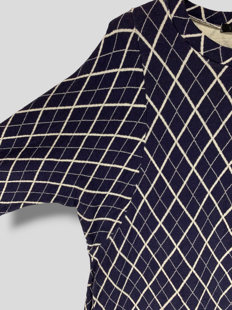 May include: Navy blue sweater with a white diamond pattern. The sweater has long sleeves and a crew neck. The argyle-like design covers the entire garment. The fabric appears to be a knit material.