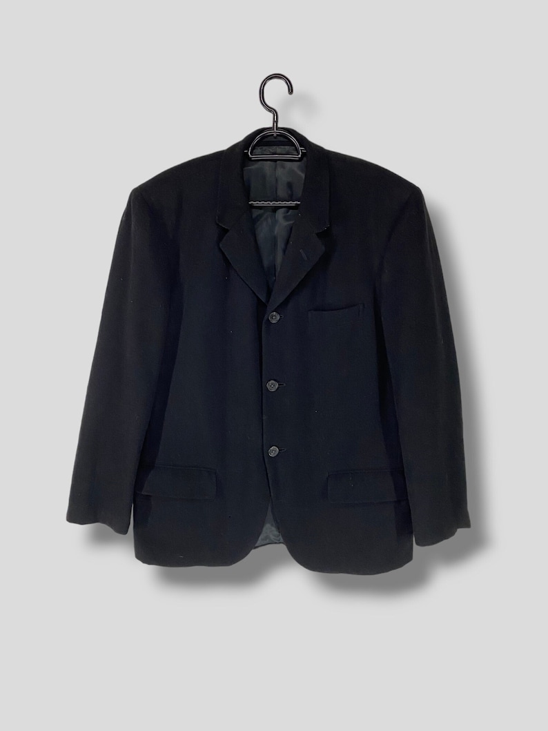 May include: A black blazer with a three-button closure and a single pocket on the left side.