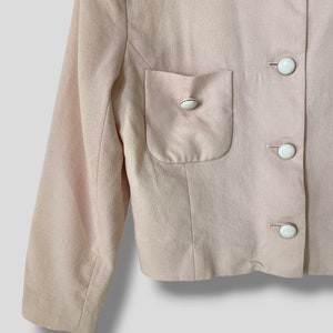 May include: A pale pink blazer with a single patch pocket on the left side. The blazer has a button-up front closure with five white buttons.