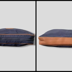 May include: Navy blue travel bag with a brown leather bottom and trim. The bag has a zipper closure and a small leather patch. The bag is shown from two different angles.