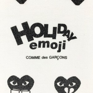 Puede incluir: Tela blanca con corazones gr&aacute;ficos negros y texto. El texto dice "HOLIDAY emoji" encima de "COMME des GAR&Ccedil;ONS". Los corazones tienen varios dise&ntilde;os de ojos y bocas, incluyendo un coraz&oacute;n roto y un coraz&oacute;n leyendo un libro.