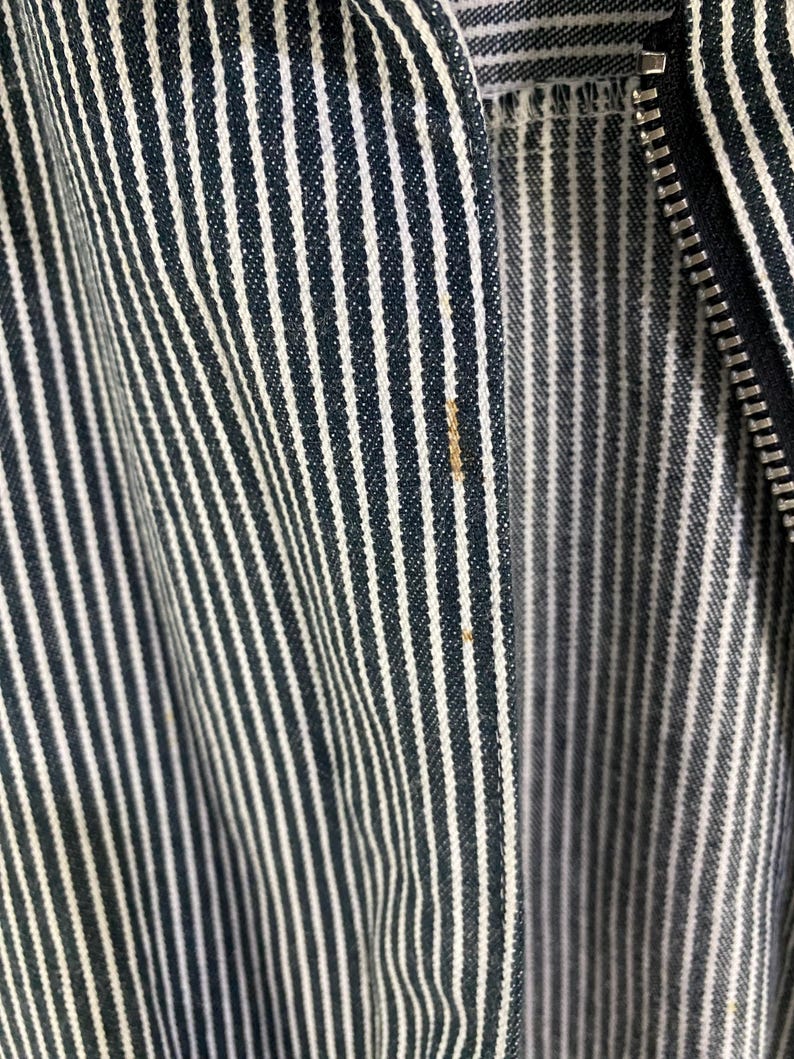 May include: Close-up of a black and white striped fabric with a zipper. The fabric is woven with thin black stripes and wider white stripes.
