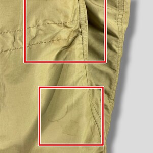 Puede incluir: Primer plano de una tela de color beige, posiblemente una secci&oacute;n de pantal&oacute;n o chaqueta. La tela tiene costuras visibles y un detalle de bolsillo. Hay algunas manchas y marcas en el material, lo que indica desgaste. El fondo es un degradado de gris claro.