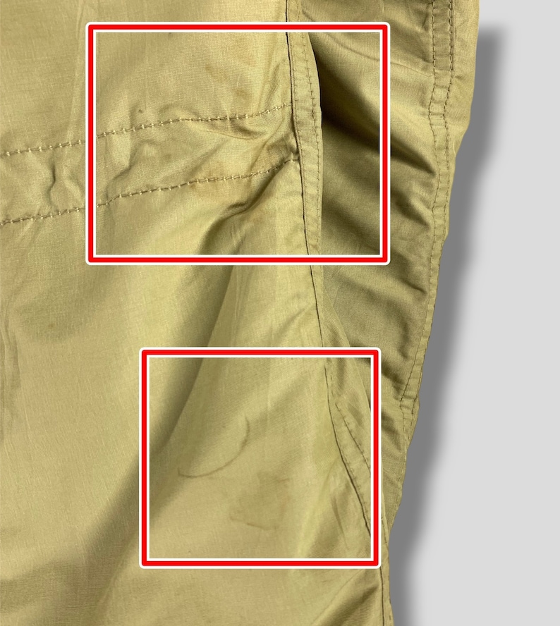 Puede incluir: Primer plano de una tela de color beige, posiblemente una secci&oacute;n de pantal&oacute;n o chaqueta. La tela tiene costuras visibles y un detalle de bolsillo. Hay algunas manchas y marcas en el material, lo que indica desgaste. El fondo es un degradado de gris claro.
