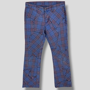 Può includere: Pantaloni a quadri blu e rossi caratterizzati da un design patchwork con cuciture sfilacciate visibili. Il capo presenta una vita standard con chiusura a bottone, passanti per cintura e una costruzione a pannelli che crea un motivo.