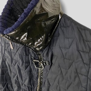 May include: A black quilted jacket with a black patent leather collar and a zipper closure. The jacket has a diamond-shaped quilted pattern.
