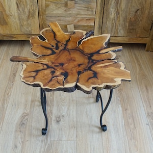 May include: A small, round, wooden table with a natural wood finish and black metal legs. The table top is a single piece of wood with a unique, organic shape.