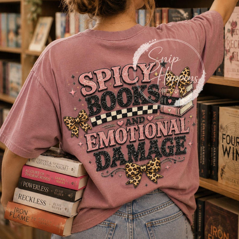 Pu&ograve; includere: T-shirt rosa antico con la scritta "Spicy Books and Emotional Damage" in un design a strati. Il design include fiocchi leopardati, cuori e un motivo a scacchi. La persona tiene in mano una pila di libri.