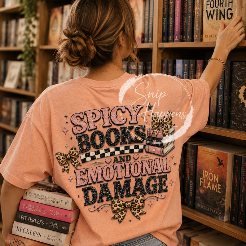 Pu&ograve; includere: Una maglietta color pesca con la scritta "SPICY BOOKS AND EMOTIONAL DAMAGE" in un font retr&ograve;. Il design include fiocchi con stampa leopardata e una pila di libri. La persona tiene in mano una pila di libri.