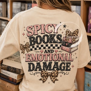 Pu&ograve; includere: T-shirt color crema con la scritta "Spicy Books and Emotional Damage" in rosa e nero. Il design include fiocchi con stampa leopardata, una pila di libri e un motivo a scacchi.