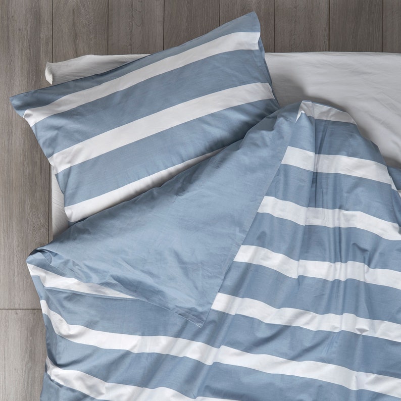 Puede incluir: Una funda n&oacute;rdica a rayas azules y blancas con una funda de almohada a juego. La funda n&oacute;rdica est&aacute; doblada sobre la funda de almohada, creando un efecto de capas.