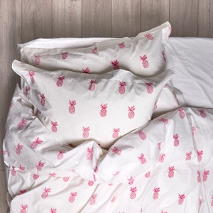 May include: White bedding with a pink pineapple pattern. The bedding includes a duvet cover, a flat sheet, and two pillowcases.