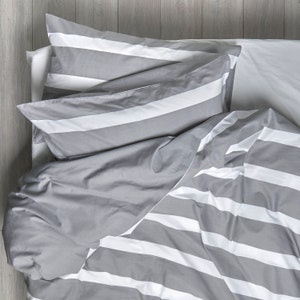 May include: A grey and white striped duvet cover with matching pillowcases. The duvet cover is folded back to reveal the white stripes underneath.
