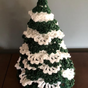 May include: A crocheted Christmas tree decoration in green and white. The tree is made of multiple layers of crocheted circles, creating a layered effect.