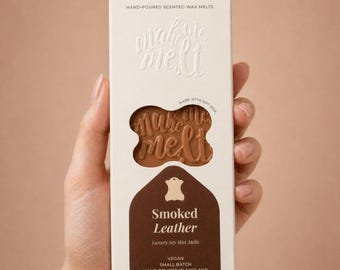 May include: A rectangular white cardboard box of hand-poured scented soy wax melts. The packaging features the text "make me melt" and "Smoked Leather Luxury Soy Wax Melts" with a cutout window revealing the brown wax bar embossed with text.