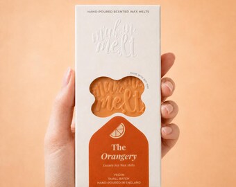 May include: A rectangular white cardboard box containing orange wax melts. The packaging features the text "make me melt" and "The Orangery Luxury Soy Wax Melts" with a small orange slice icon. The box indicates it is vegan, small batch, and hand-poured.