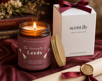 May include: A lit amber glass candle with a maroon label reading "Smells like you're going to... The University of Leeds" and "Well done Charlie". Beside it sits a white gift box with a maroon ribbon and a rolled parchment diploma with a gold seal.
