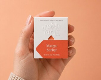 May include: A square white cardboard box containing hand-poured scented wax melts. The packaging features the embossed text "make me melt" and a bright orange label with the printed text "Mango Sorbet" and "Luxury Soy Wax Melts" in white.
