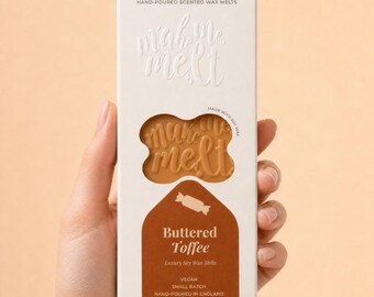 May include: A rectangular white cardboard box containing buttered toffee scented soy wax melts. The packaging features the text mah me melt, a cutout window revealing the tan wax, and a brown label with the text Buttered Toffee and Vegan.