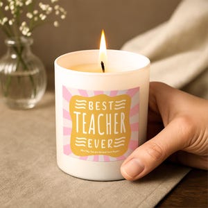 Könnte beinhalten: Eine weiße Kerze in einem Glasgefäß mit brennendem Docht. Das Etikett zeigt ein gelbes, gewelltes Rechteck auf einem rosa-weißen Strahlenhintergrund mit dem Text "BEST TEACHER EVER" und "Mrs Tilly: You are the best! Love Rypers" in Weiß.