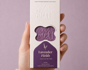 May include: A rectangular white cardboard box containing purple lavender-scented soy wax melts. The packaging features the text "make me melt" and "Lavender Fields" with a cutout window revealing the embossed wax. It is labeled vegan and small batch.