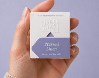 May include: A square white cardboard box containing scented wax melts. The packaging features the embossed text "make me melt" and a purple label with the white printed text "Pressed Linen" and "Luxury Soy Wax Melts" at the bottom.