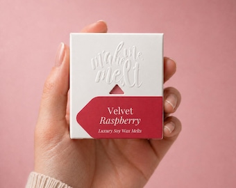 May include: A square white cardboard box featuring the embossed text make me melt. A dark pink label at the bottom displays the white text Velvet Raspberry and Luxury Soy Wax Melts. The packaging has a small triangular cutout above the label.