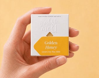 May include: A square white cardboard box containing hand-poured scented wax melts. The packaging features the embossed text "make me melt" and a yellow label with the printed text "Golden Honey" and "Luxury Soy Wax Melts" in white font.