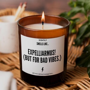 May include: A lit candle in a brown glass jar with a white label that reads SCENTILY SMELLS LIKE... EXPELLIARMUS! (BUT FOR BAD VIBES.) with a lightning bolt icon and the text add your optional message here... printed on the front of the container.