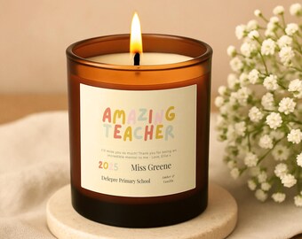 Op de afbeelding: Een brandende kaars in een bruine glazen pot met een wit etiket met de tekst Amazing Teacher, I'll miss you so much! Thank you for being an incredible mentor to me - Love, Ellie x, 2025, Miss Greene, Delepre Primary School, Amber & Vanilla.
