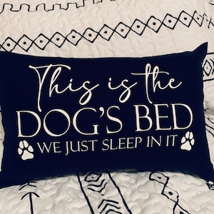 May include: A black pillow with white text that reads "This is the Dog's Bed We Just Sleep In It" with a paw print on either side of the text.