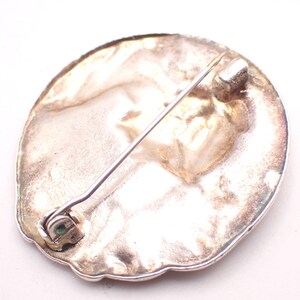 K&ouml;nnte beinhalten: Silberfarbene Brosche mit Nadelverschluss. Die Brosche hat eine ovale Form mit strukturierter Oberfl&auml;che und dekorativem Rand. Die Nadel ist auf der R&uuml;ckseite der Brosche befestigt.