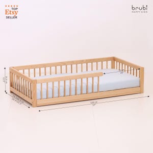 May include: A light-colored wooden toddler bed with a light blue mattress. The bed frame has a slatted design on the sides and headboard. The bed is 57 inches long, 20 inches wide, and 12.5 inches high. The Etsy seller logo is in the top left corner.
