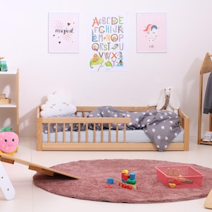 May include: A child's bedroom scene featuring a wooden bed with a gray star-patterned comforter and a cloud-shaped pillow. The room includes a pink rug, colorful toys, and decorative posters with the words "magical" and "cute".