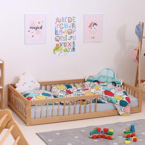 May include: A wooden toddler bed with a light blue mattress, colorful bedding, and decorative pillows shaped like a cloud and a car. The room features framed artwork and a wooden toy train on a gray rug.