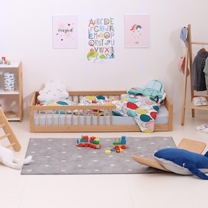 May include: A child's bedroom with a wooden bed, a gray rug with white polka dots, and colorful bedding. The room is decorated with framed artwork and a wooden clothing rack. Toys, including a train and a whale, are scattered on the rug.