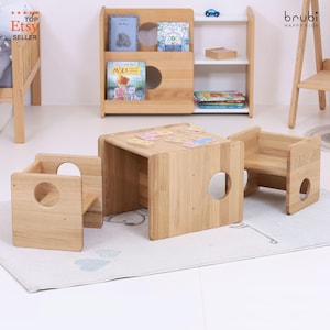 Puede incluir: Un juego de muebles infantiles de madera clara, que incluye una mesa pequeña y dos sillas, con una estantería a juego en el fondo. La mesa tiene azulejos de colores en la parte superior. Muebles infantiles.