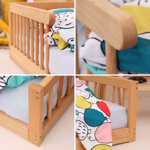 May include: A small wooden crib with a light-colored finish. The crib features a slatted side and a headboard and footboard. The crib is furnished with a white sheet and a patterned blanket with colorful balloons.