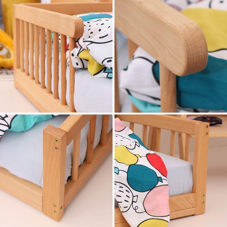 May include: A small wooden crib with a light-colored finish. The crib features a slatted side and a headboard and footboard. The crib is furnished with a white sheet and a patterned blanket with colorful balloons.