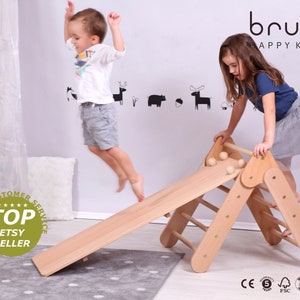 Puede incluir: Un triángulo de escalada de madera con tobogán, diseñado para niños. La imagen muestra a dos niños interactuando con el juguete. La marca "brubi HAPPY KIDS" es visible. También aparece el texto "TOP ETSY SELLER".