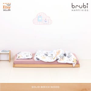 Könnte beinhalten: Ein niedriges Holzbett mit einer staubrosa Matratze, einer gemusterten Bettdecke und einem passenden Kissen. Die Bettdecke und das Kissen weisen einen skurrilen Tierdruck auf. Das Bett ist für Kinder konzipiert.