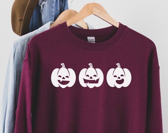 May include: Burgundy sweatshirt with a white graphic of three smiling jack-o'-lantern pumpkins.