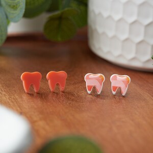 May include: Four tooth-shaped earrings, two are solid orange and two are white with an orange swirl design.