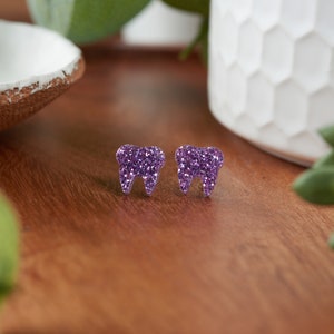 May include: A pair of purple glitter tooth-shaped stud earrings.