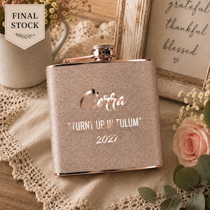 Könnte beinhalten: Ein roségoldener Metallflachmann mit Glitzer-Finish, graviert mit dem Namen Cierra, dem Text "TURNT UP IN TULUM" und dem Jahr 2027. Der Flachmann hat einen Schraubverschluss und eine rechteckige Form mit metallischem Glanz auf der texturierten Oberfläche.