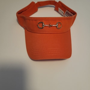 May include: Orange visor with a gold metal horse bit detail.