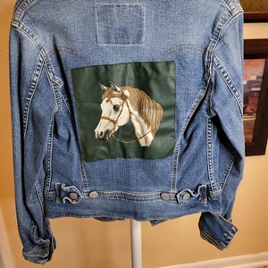 May include: A blue denim jacket with a green and white embroidered horse patch on the back.