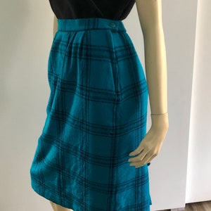 May include: A teal blue plaid skirt with a black waistband and a single button fastening. The skirt is knee-length and has a straight silhouette.