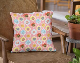 Könnte beinhalten: Ein rosa Kissen mit einem geometrischen Muster aus bunten Kreisen und Tropfenformen. Das Kissen liegt auf einem braunen Ledersessel.
